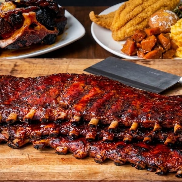 A rack of BBQ ribs with sides of fried fish, mac and cheese, collard greens, and sweet potatoes.
